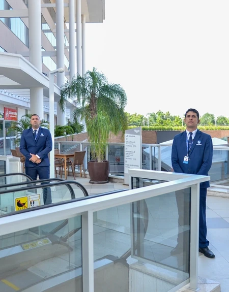 Seguranças executivos uniformizados em ambiente moderno de shopping ou prédio corporativo.